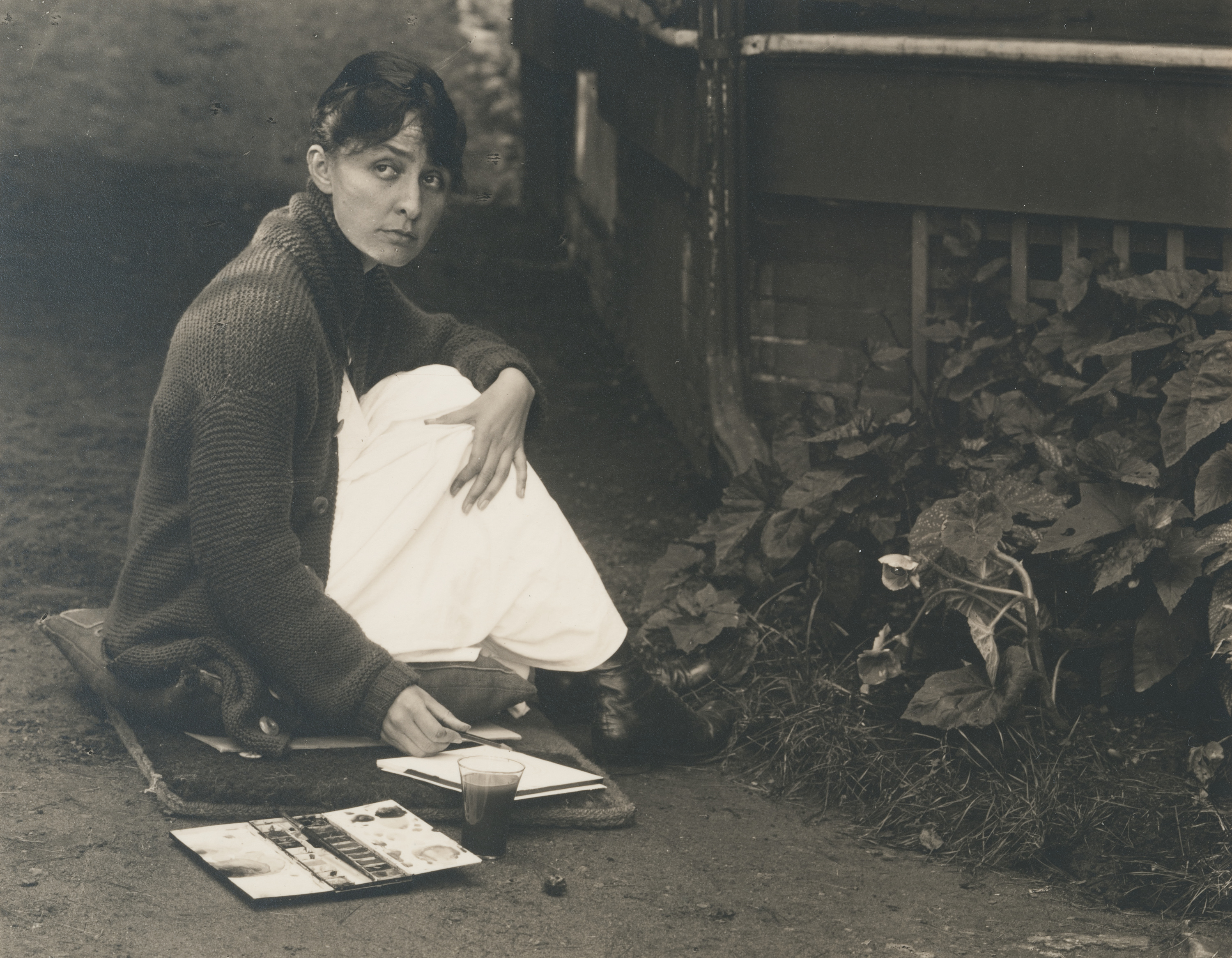 Black and white photograph of Georgia O'Keeffe sitting in the garden with her sketchbook.