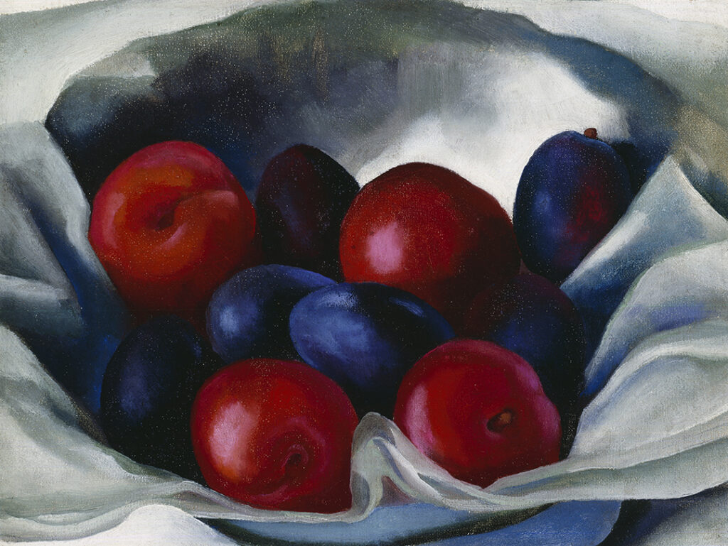 Oil still-life of an assortment of deep read and dark purple plums in a bowl laying in what appears to be a soft light paper or cloth