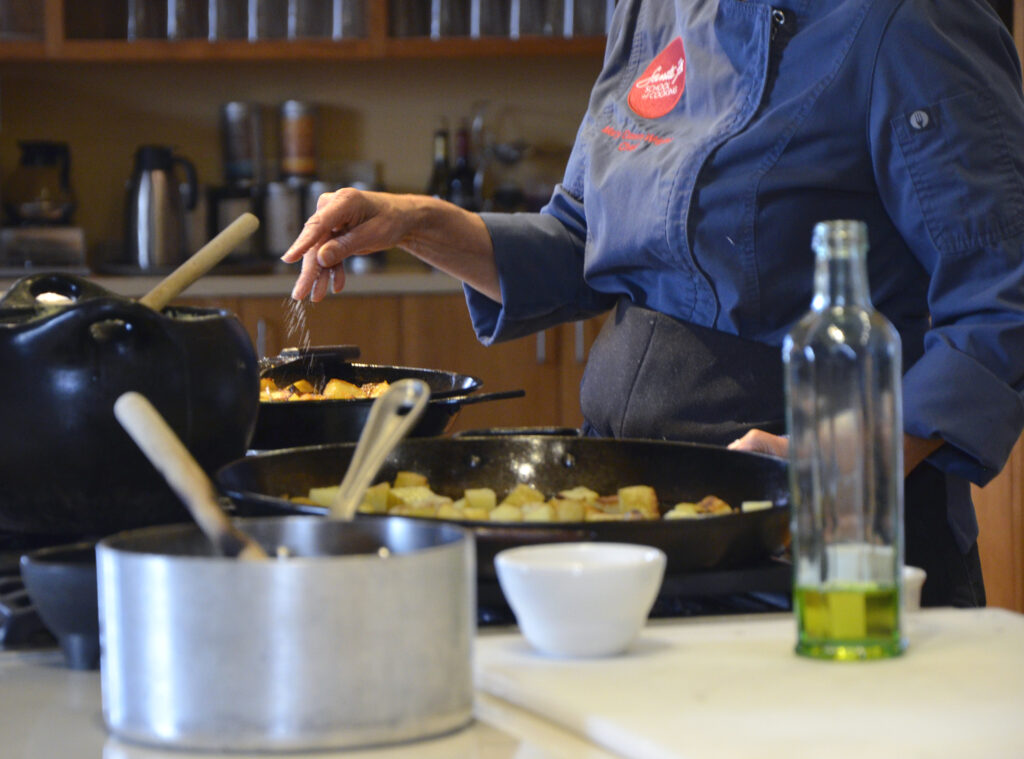 A chef's hand as they season potatoes in a cast-iron skillet.