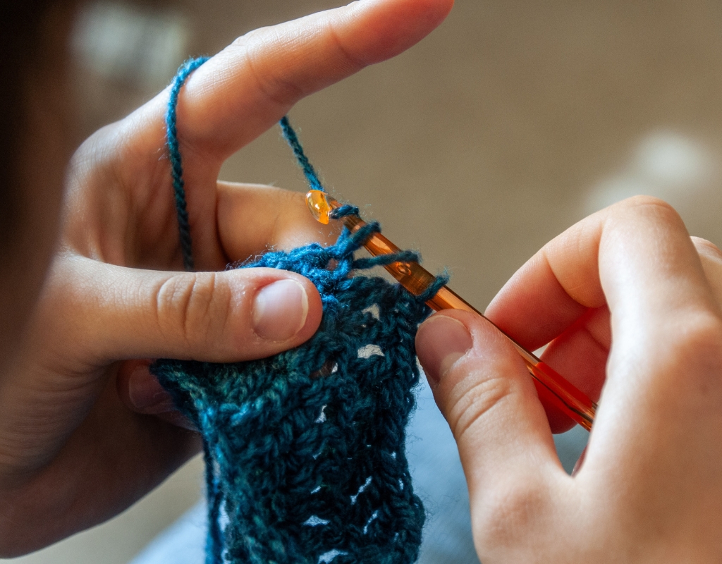 Photograph of a person's hands as they crochet with blue yarn.