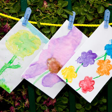 Three paintings drying on a clothesline, most are of colorful flowers