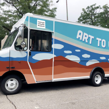 Image of a truck with 'Art to G.O' on it, the Musem's logo and colorful desert landscape and sky designs.
