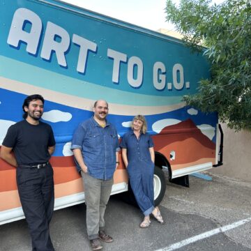 Three people smiling and standing in front of the Art to G.O. Art Truck with clouds motifs on it. On the right is the edge of a leafy green tree.