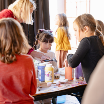 Photograph of a group of children and an adult standing over a table as they work on creative activities with paint.