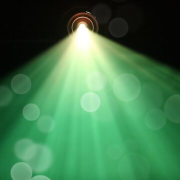 The green and yellow light of a project streams out against a dark background.