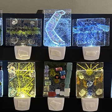 Photograph of two rows of small night lights with colorful glass designs in shades of blue, green, and yellow.