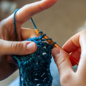 Photograph of a person's hands as they crochet with blue yarn.