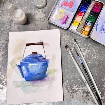 Photograph of a small painting of a blue tea kettle. Near the painting rests a colorful paint palette and some small brushes.