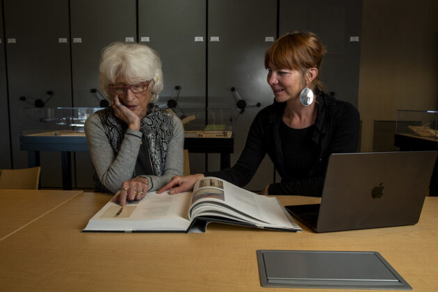 Photograph of two people sitting at a table looking at a large book.