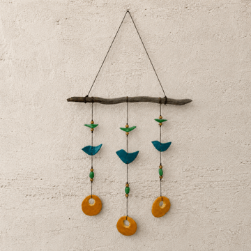 A mobile art piece made of a piece of wood from which hang small circular and bird-shaped pieces of glass.