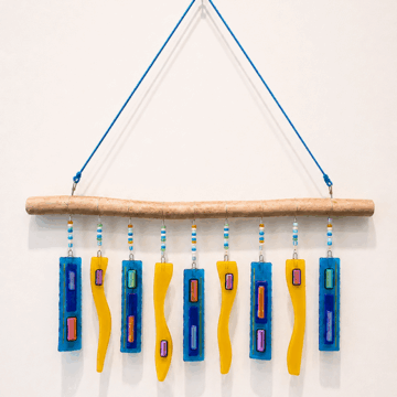 A mobile art piece made of a piece of wood from which hang small pieces of glass.