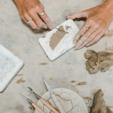 Photo from above of hands working with clay. Nearby lay tools.
