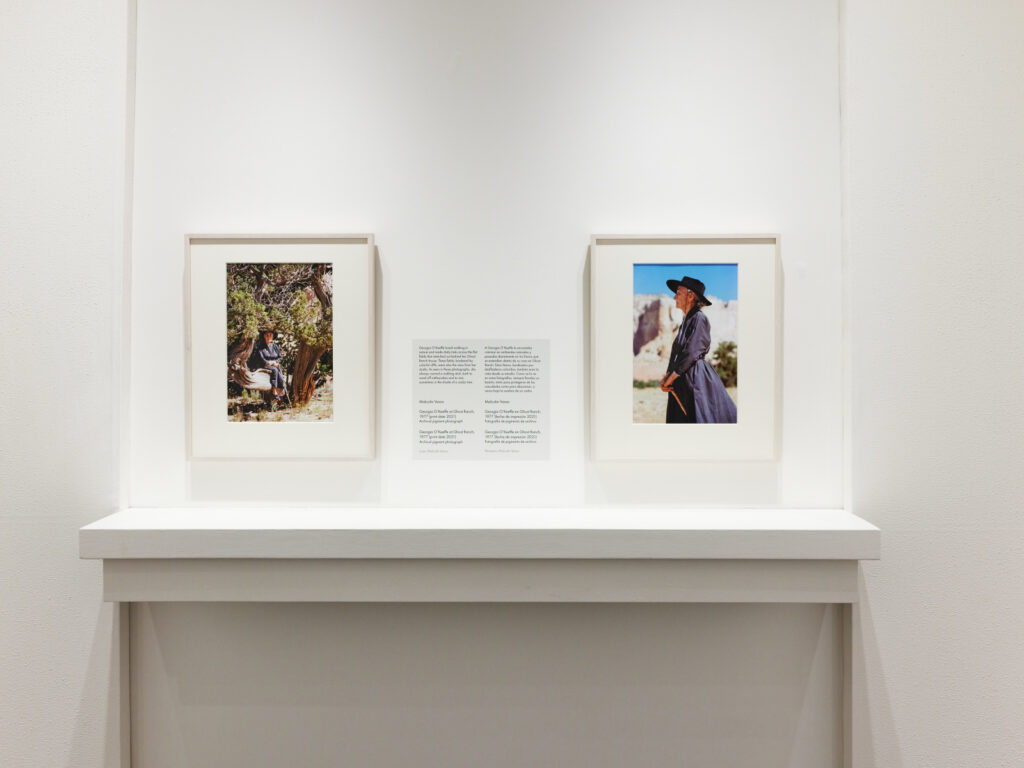 A view of a gallery with white walls and two framed color photographs and a text panel. The room has a dark brown floor.