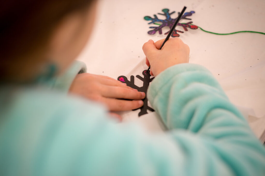 5. Closeup Photograph of a child painting wooden snowflake ornaments. The child is blurred and the camera is focused on their handiwork.