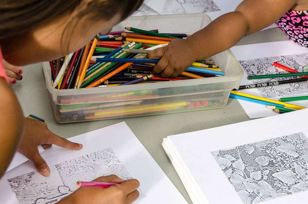 Close-up photograph of young people bent of drawing with a box of multiples color pencils.