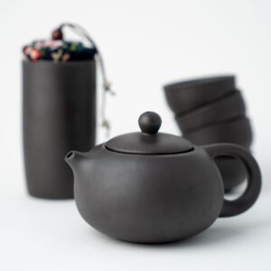 Dark grey tea pot with stack of cups and container in the background