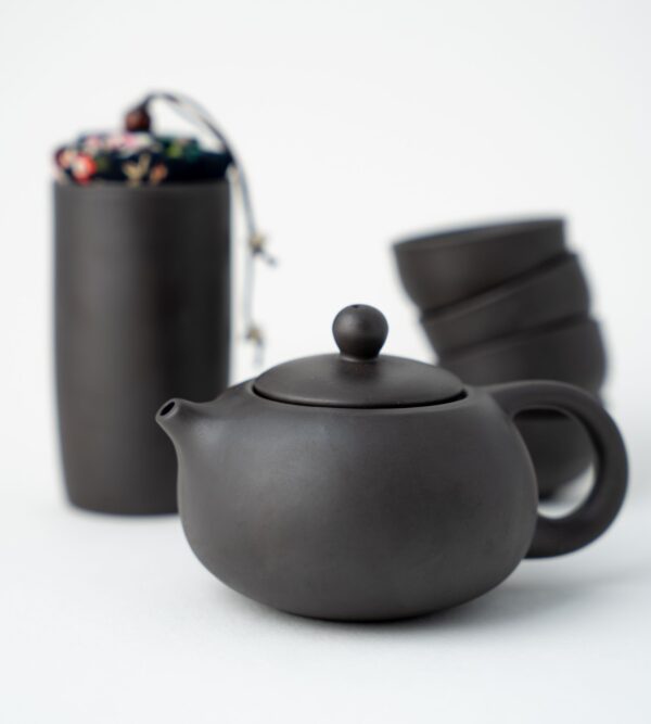 Dark grey tea pot with stack of cups and container in the background