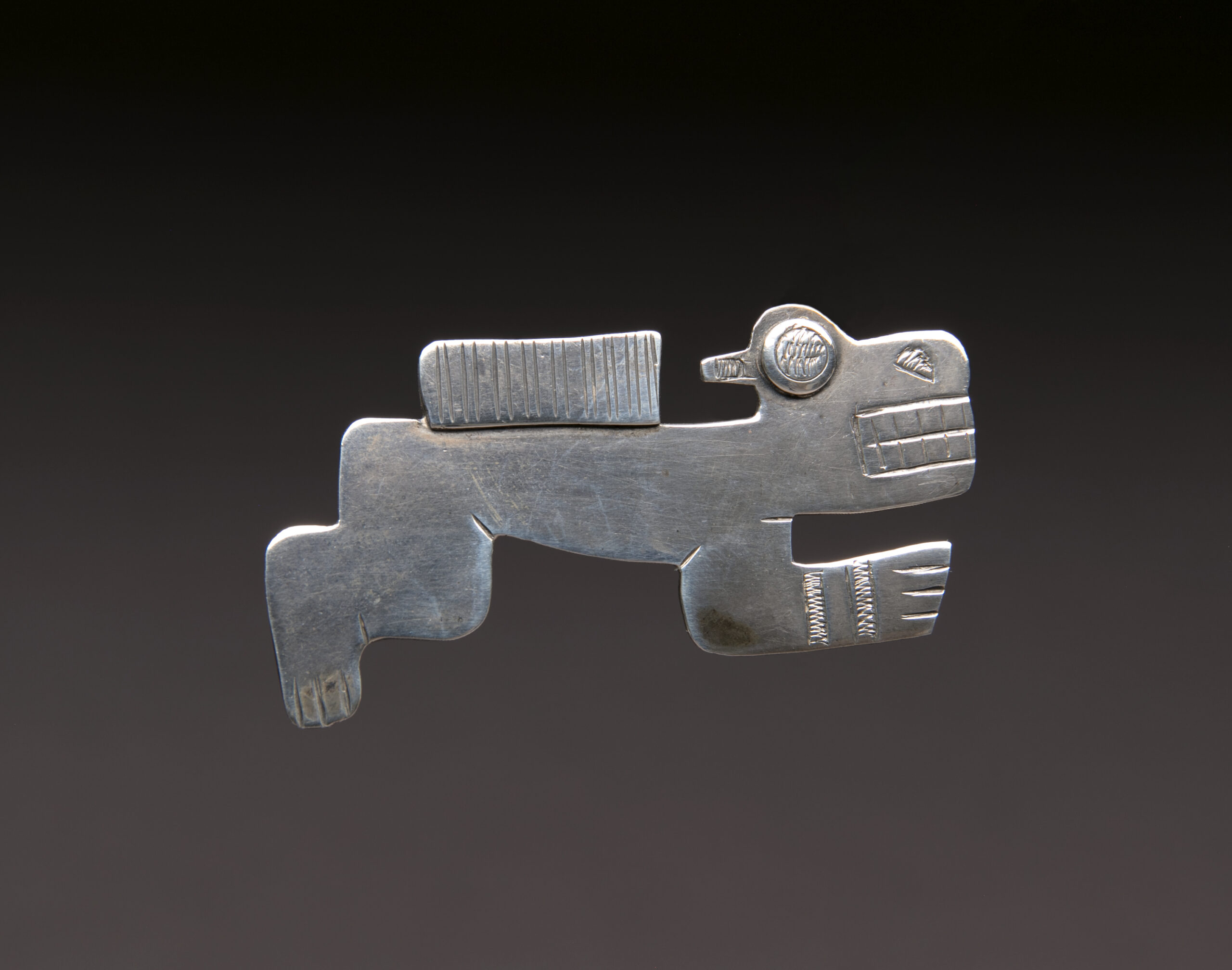 Pre-Columbian style silver pin in shape of a stylized reclining animal, engraving and carving on surface.