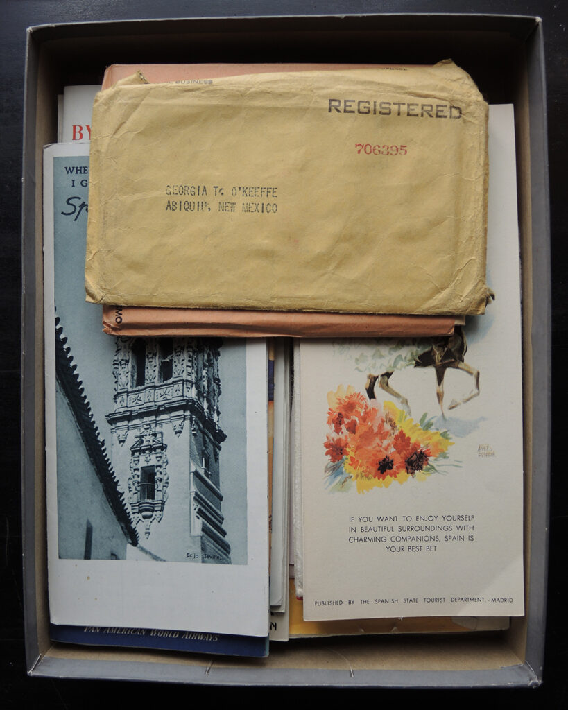 A box filled with pamphlets about traveling to Spain. On the top is an envelope addressed to O'Keeffe in Abiquiú