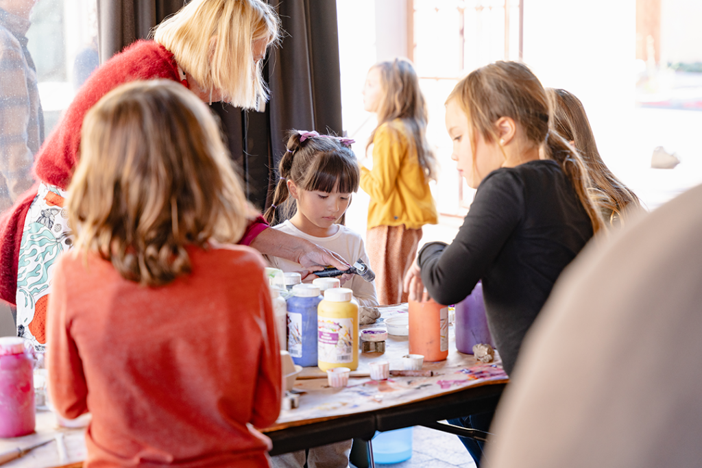 Photograph of a group of children and an adult standing over a table as they work on creative activities with paint.