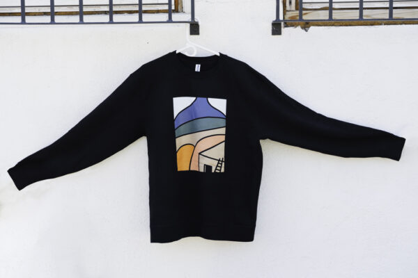 A black sweatshirt hanging with a simple modern design of a desert landscape and adobe home in shades of blue, beige, green, and orange.