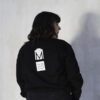 Person with dark hair wearing a black sweatshirt with their back turned to the camera.