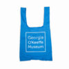 A reusable bag in blue with the Georgia O'Keeffe Museum Logo on it.