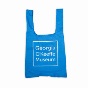 A reusable bag in blue with the Georgia O'Keeffe Museum Logo on it.