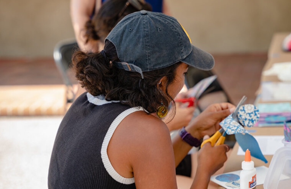 Photograph of a young person with a hat cutting a piece of paper.