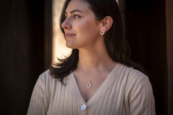 A person with dark hair wearing a silver earring and necklace inspired by the shape of a pelvis.