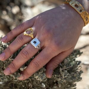Photograph of a person's hand as they were a gold cuff and two rings; one in gold and one in silver.