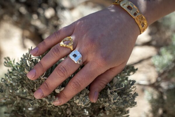 Photograph of a person's hand as they were a gold cuff and two rings; one in gold and one in silver.