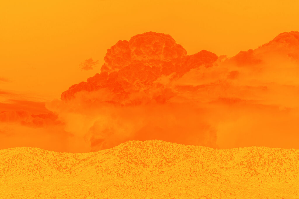 Deep dark orange clouds above the light hills of a desert landscape. The sky behind the cloud is orange and the entire canvas is bathed in orange.