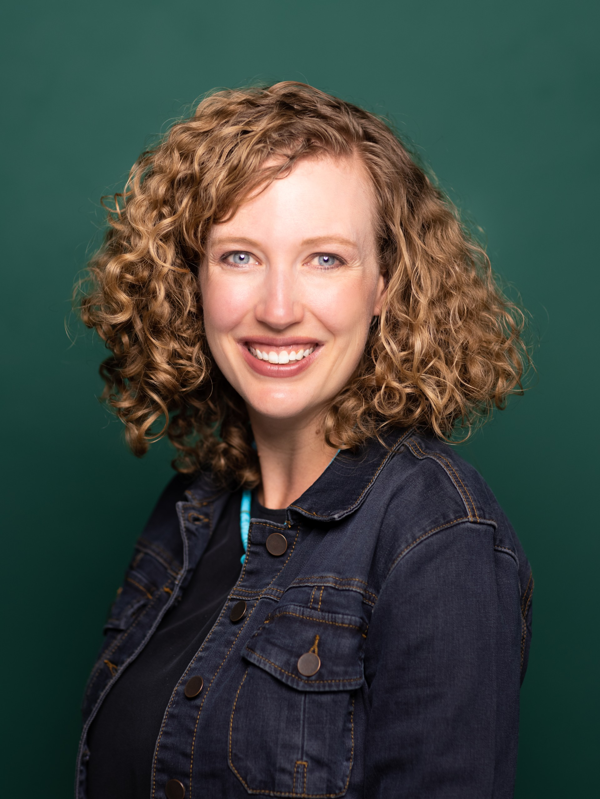 Portrait of a person with shoulder-length curly hair and smiling at the camera. 