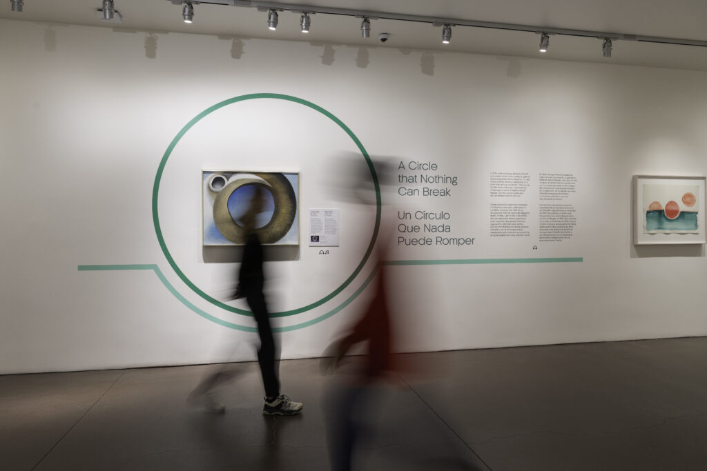An exhibition with the blurry shapes of two people walking in front.