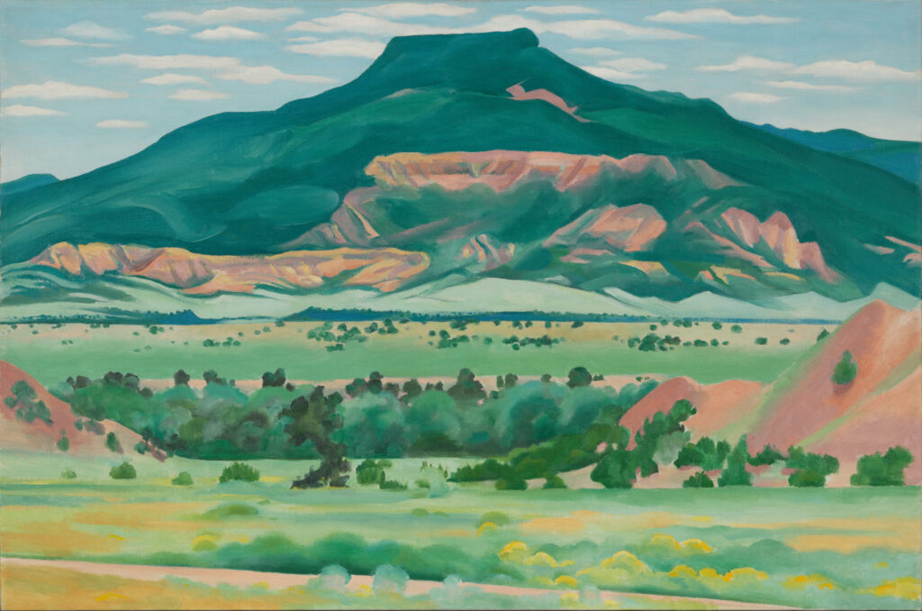 Pedernal rises up over the New Mexico landscape. Much of the mountain is covered in various shades of green. Shrubs dot the landscape in the fore- and middle-ground.