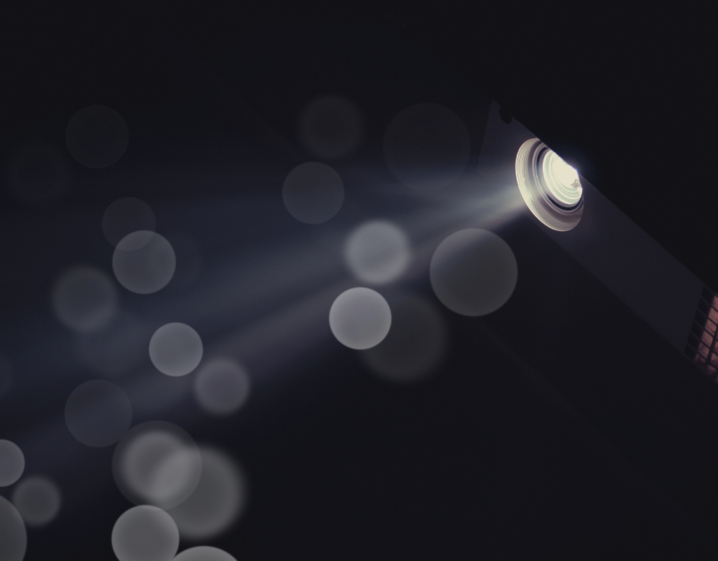 The light coming from the round opening of a projector. Small round circles of light fill the dark background.