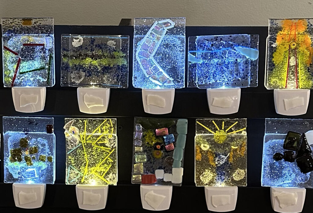 Photograph of two rows of small night lights with colorful glass designs in shades of blue, green, and yellow.