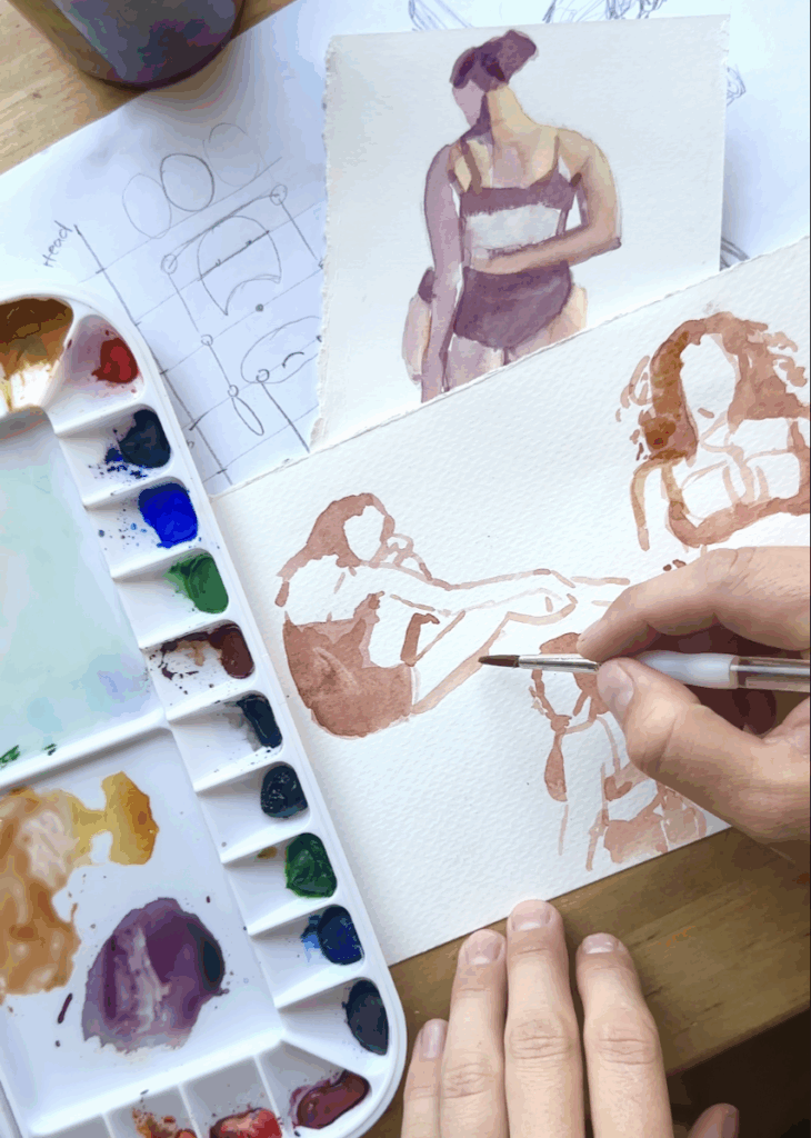 Small watercolor paintings of figures in shades of brown and purple. A hand above holds a small paintbrush. To the left is a watercolor palette.