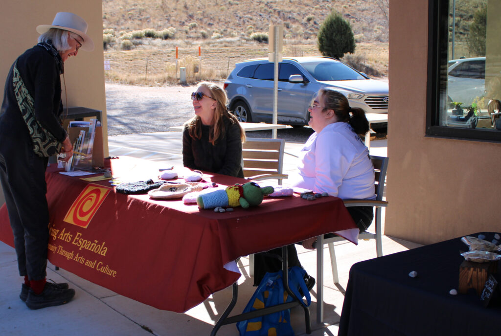Two people sit at a table while another stand above.