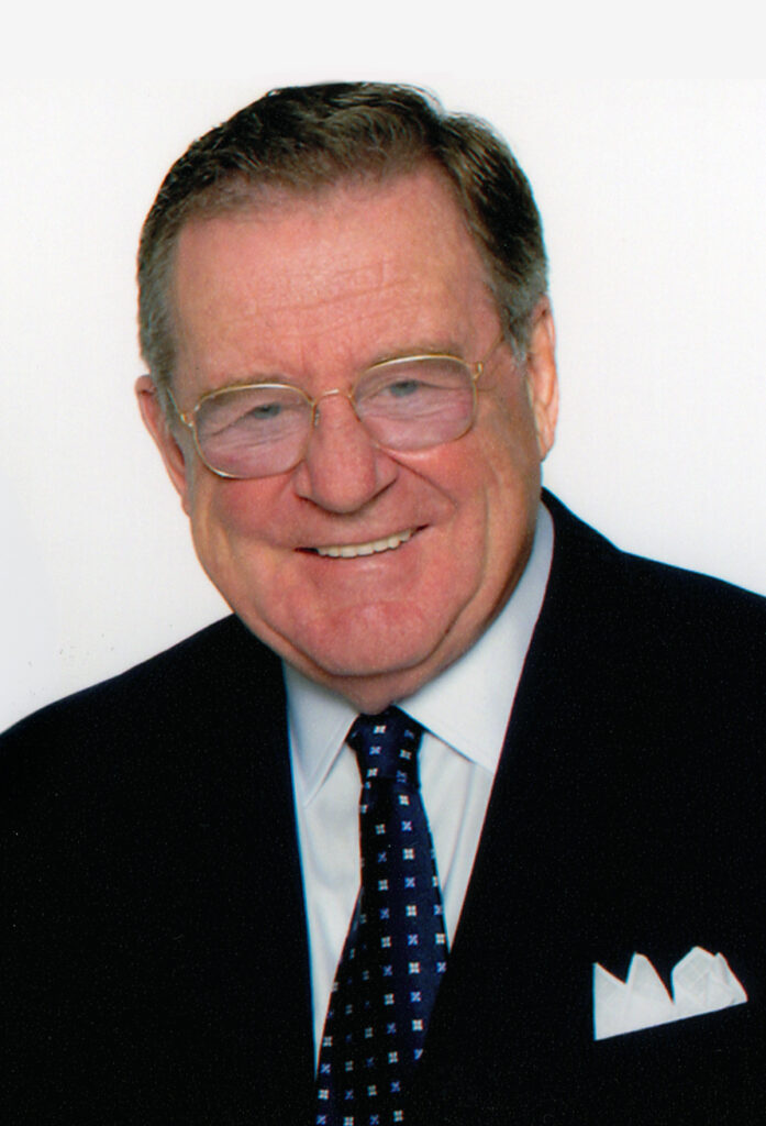 Portrait of a person in glasses and wearing a jacket and tie smiling at the camera.