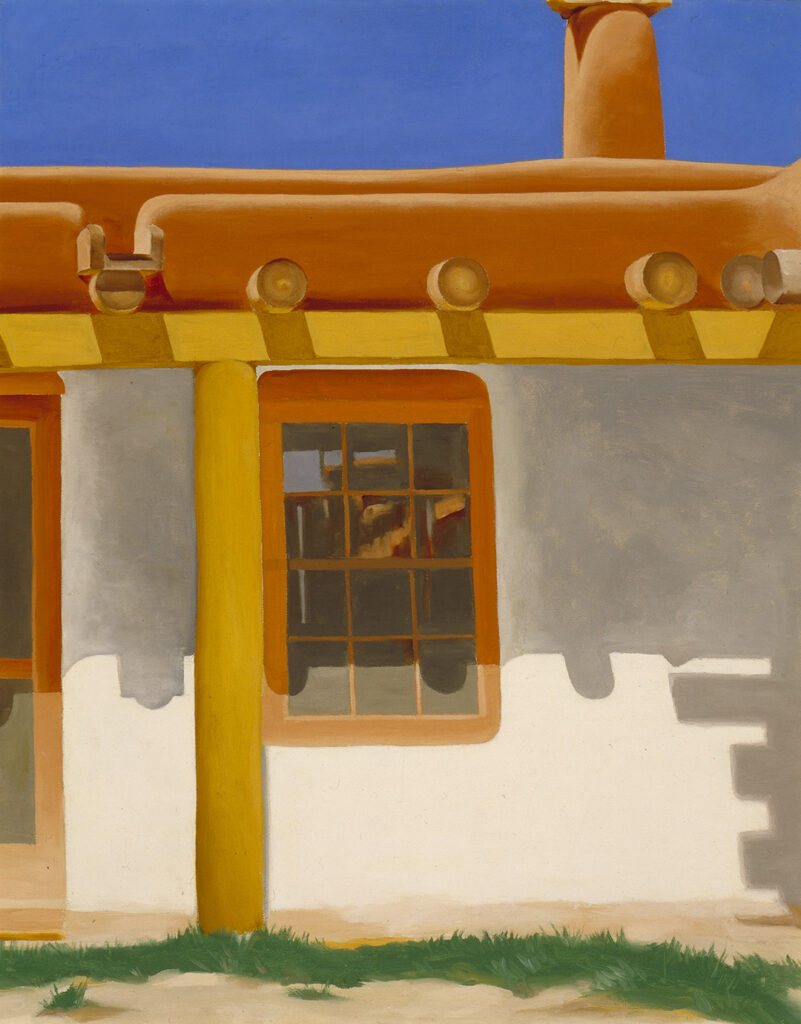 Yellowish brown support beams hold up a brown adobe patio. The patio extends from the white walls of a house, which features a window and screen door. Wooden support beams known as vigas protrude from the house's roof. A chimney emerging from the roof extends upward into a band of bright blue sky overhead.