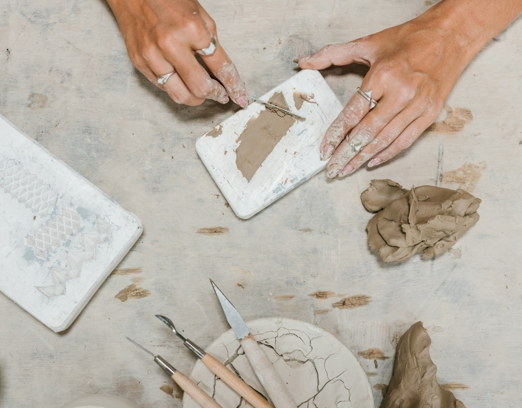 Photo from above of hands working with clay. Nearby lay tools.