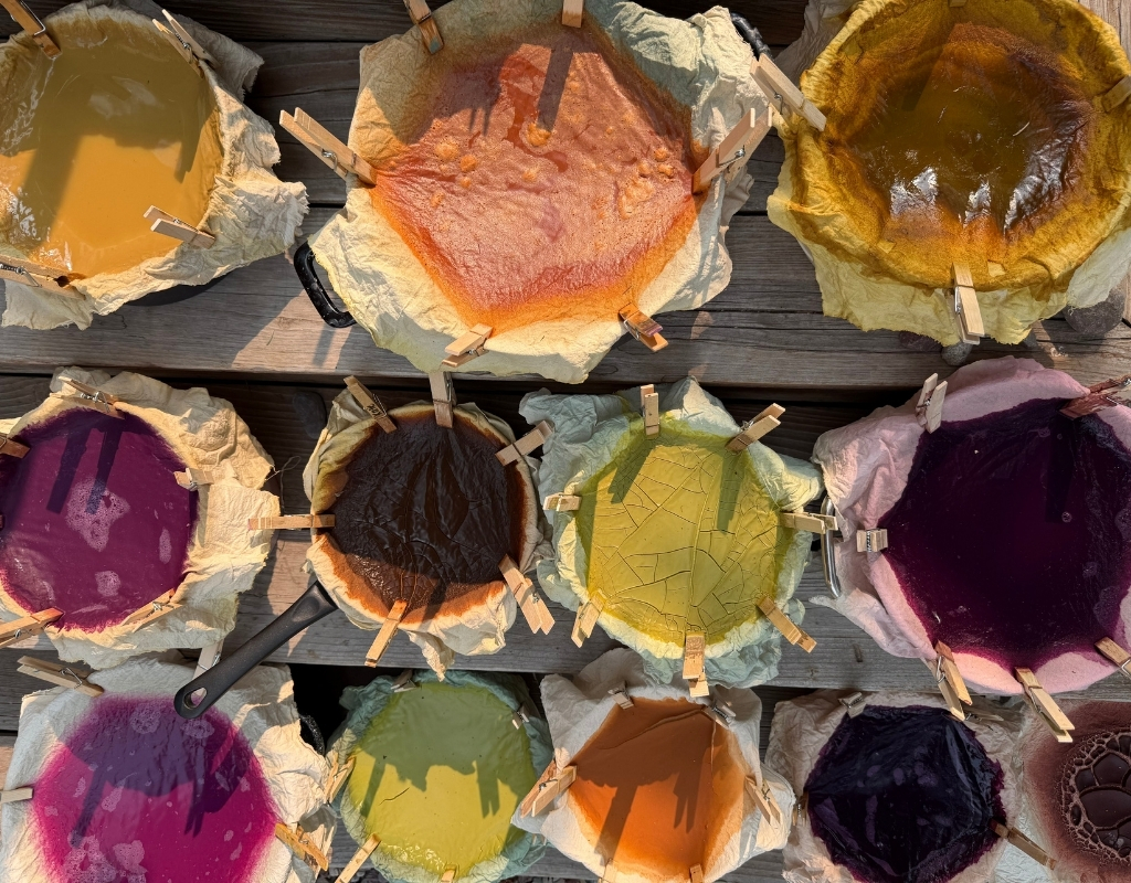Several buckets filled with various natural pigments in shades of yellow, orange, purple, and pink.