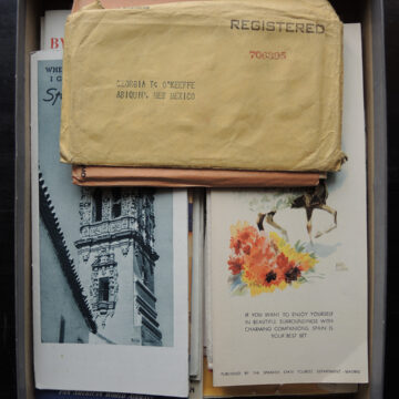 A box filled with pamphlets about traveling to Spain. On the top is an envelope addressed to O'Keeffe in Abiquiú