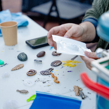 Close-up photograph of a pair of hands holding a plastic mold over a table. On the table are small colorful plastic creations.