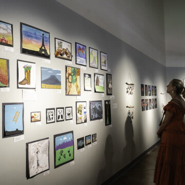 Photograph of a person looking at a gallery wall covered in artwork made by students.