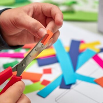 Close-up photograph of a child's hands as they cut small piece of colorful paper.