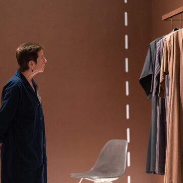 A person stands with their hands behind their back as they look at hanging clothing in an exhibition.