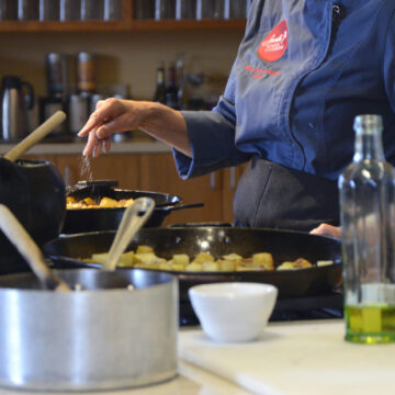 A chef's hand as they season potatoes in a cast-iron skillet.